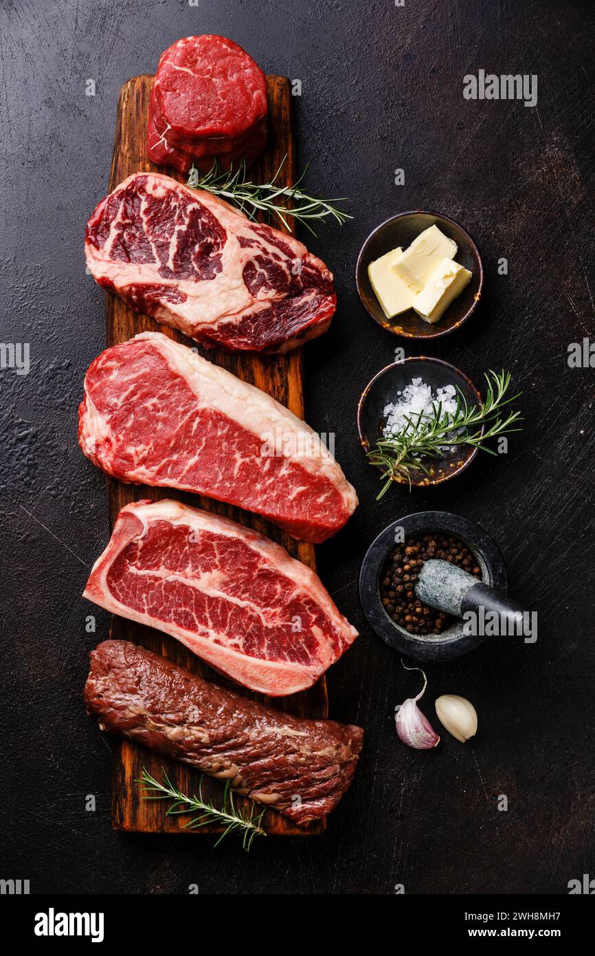 Variety of Raw Black Angus Prime meat steaks Machete, Blade on bone, Striploin, Rib eye, Tenderloin fillet mignon on wooden board and seasoning Stock Photo