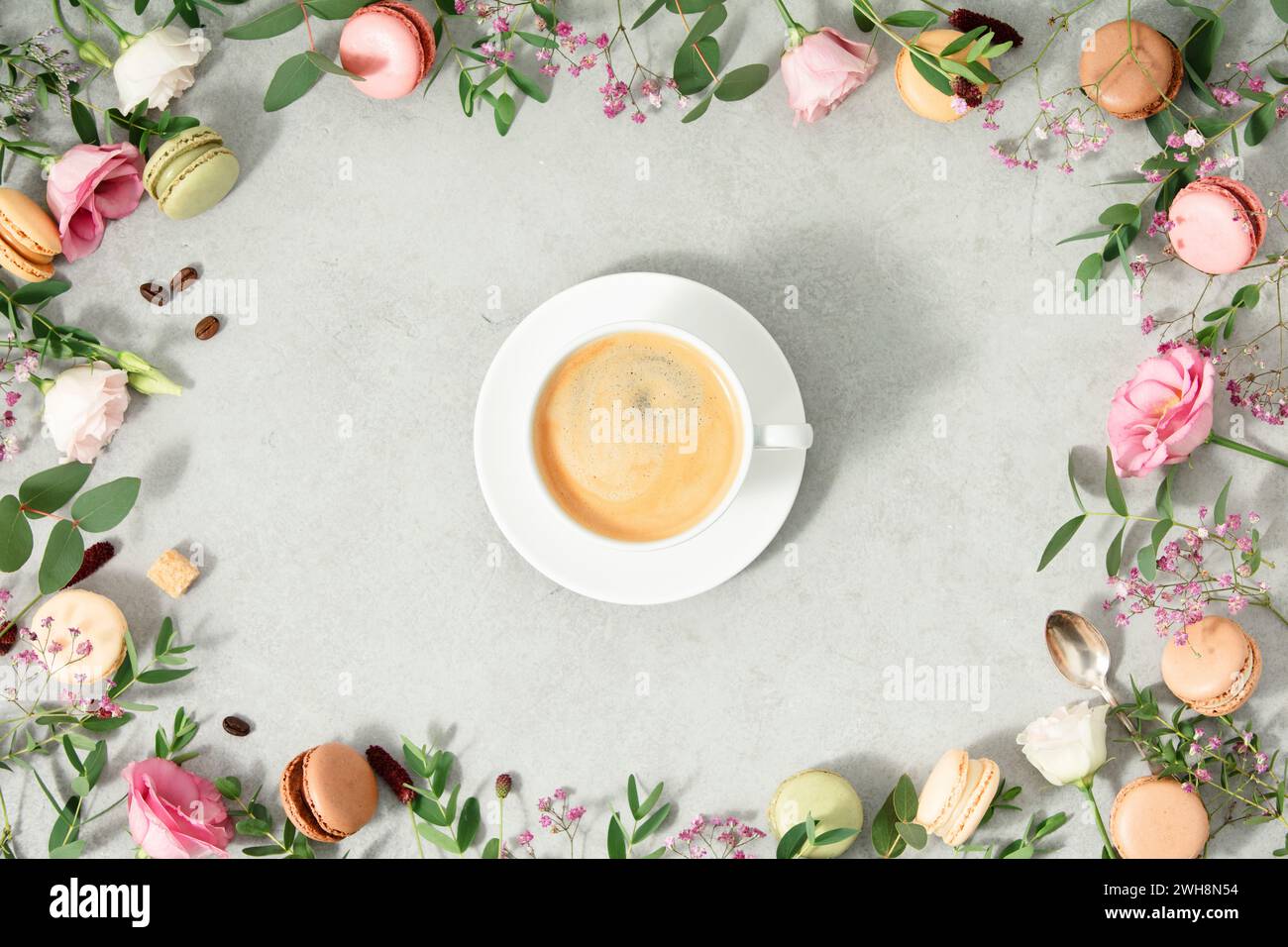 White cup of coffee and Frame made of Spring flowers and Different types of macaroons flat lay Stock Photo