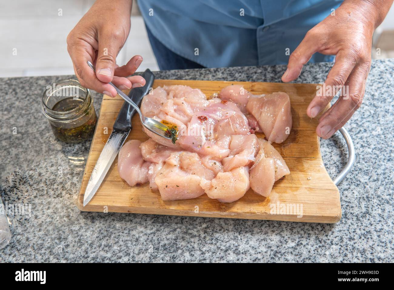 man's hands putting seasoning on a raw chicken to cook it on a cutting board Stock Photo