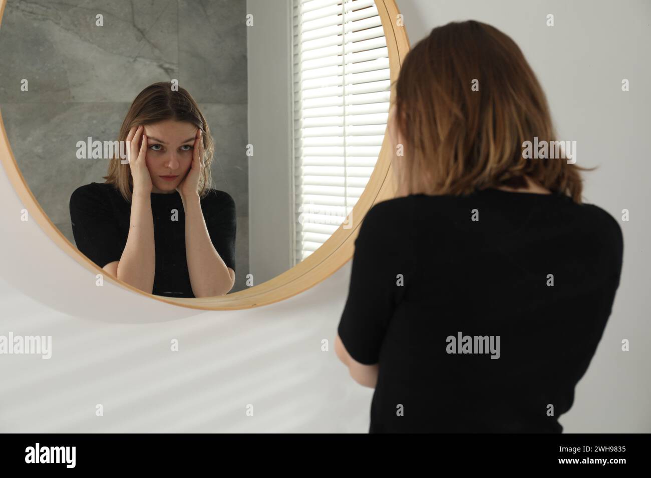 Sad young woman near mirror in room Stock Photo