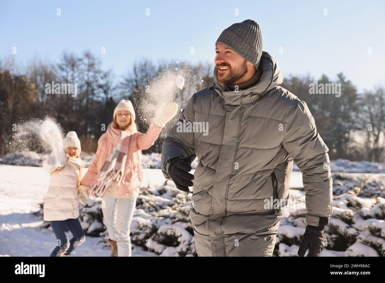 Portrait of smiling man and his family playing snowballs in winter park ...