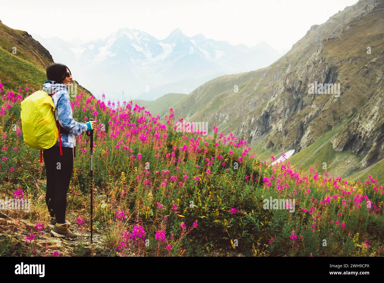 Close up smiley Caucasian woman hiker with hiking pols stand enjoy stunning mountains landscape in blooming spring nature. Solo hiking healthy lifesty Stock Photo