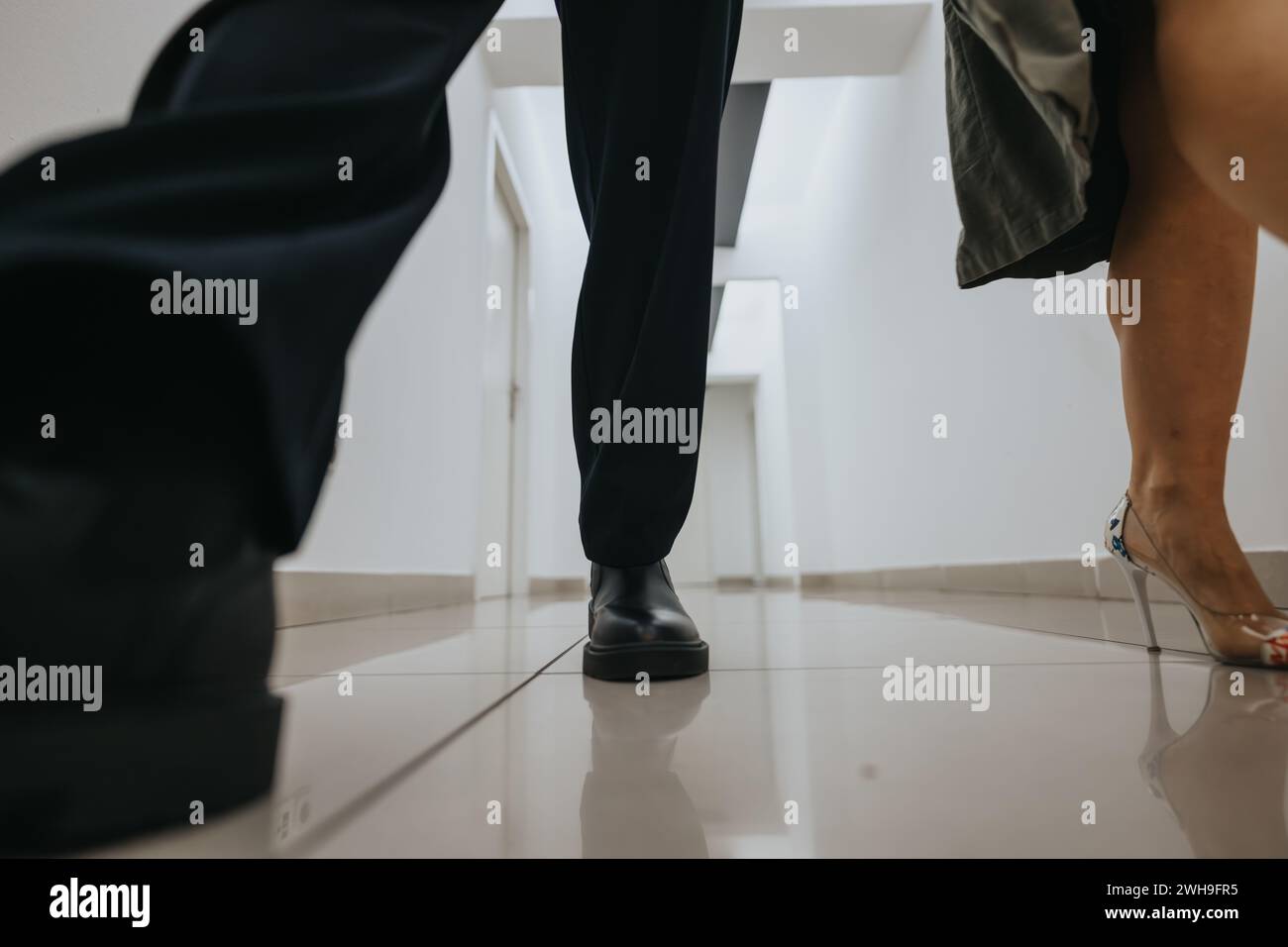 Man in black dress shoes and woman in high heels walking on a white tiled floor. Stock Photo