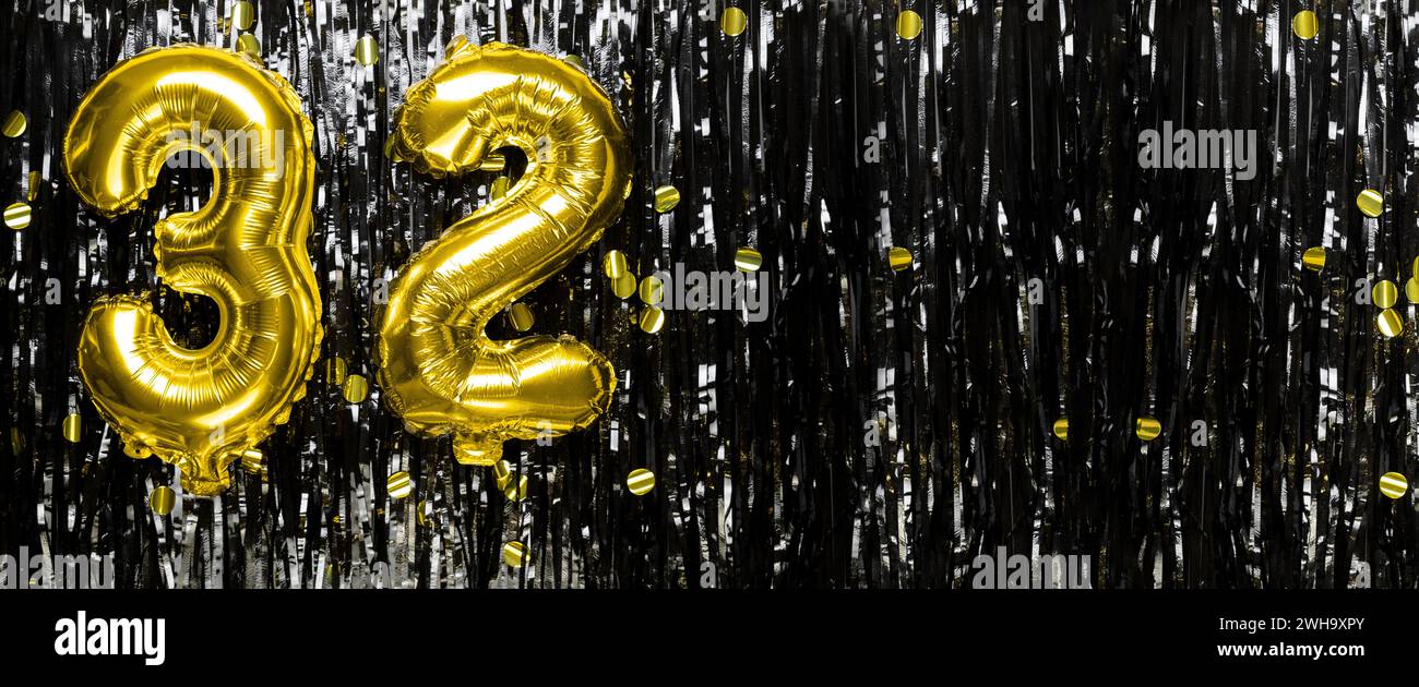 Gold foil balloon number number 32 on a background of black tinsel decoration. Birthday greeting card, inscription thirty two. Anniversary event Stock Photo
