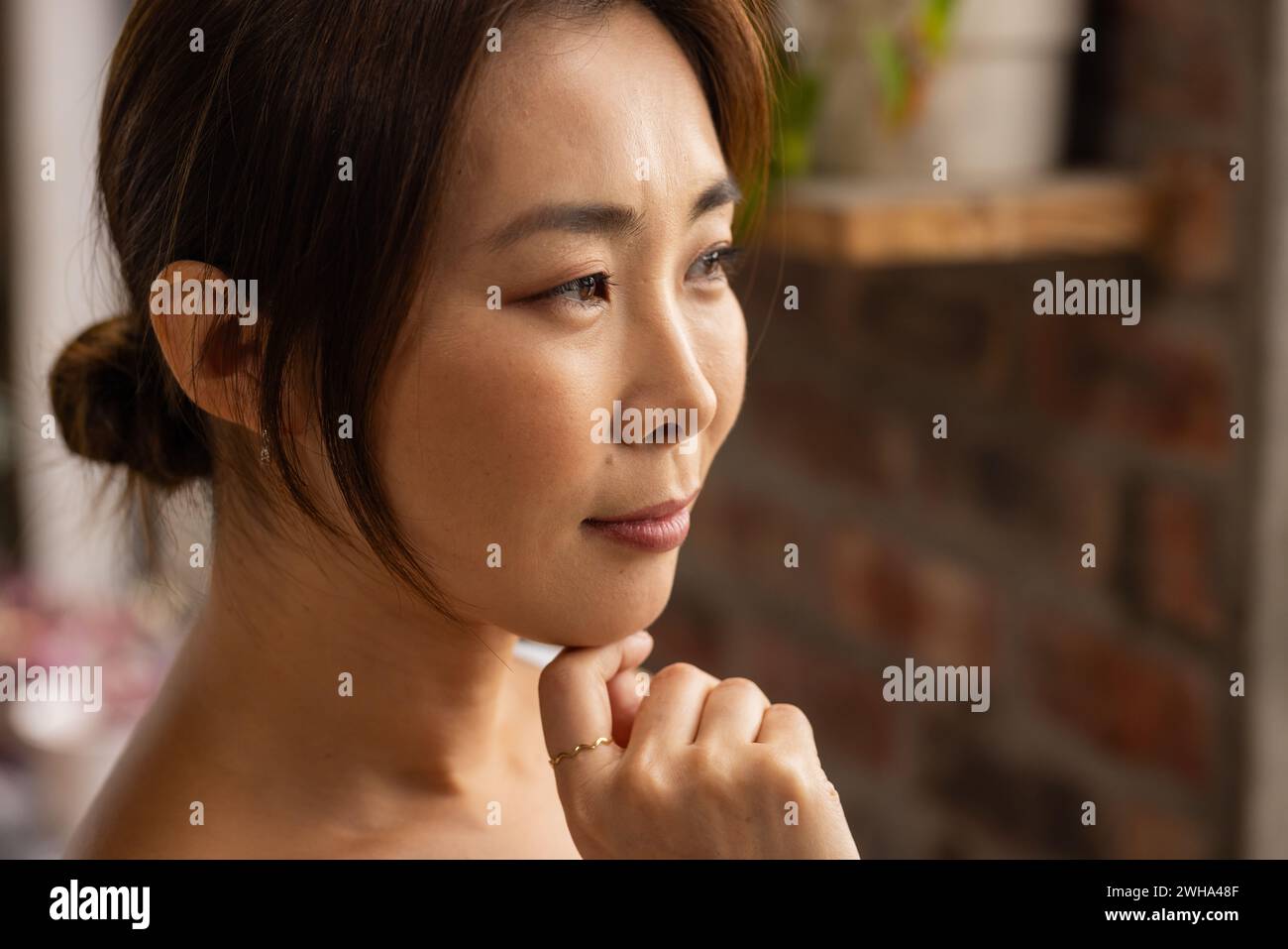Asian woman in casual business attire gazes thoughtfully in the office, with copy space Stock Photo