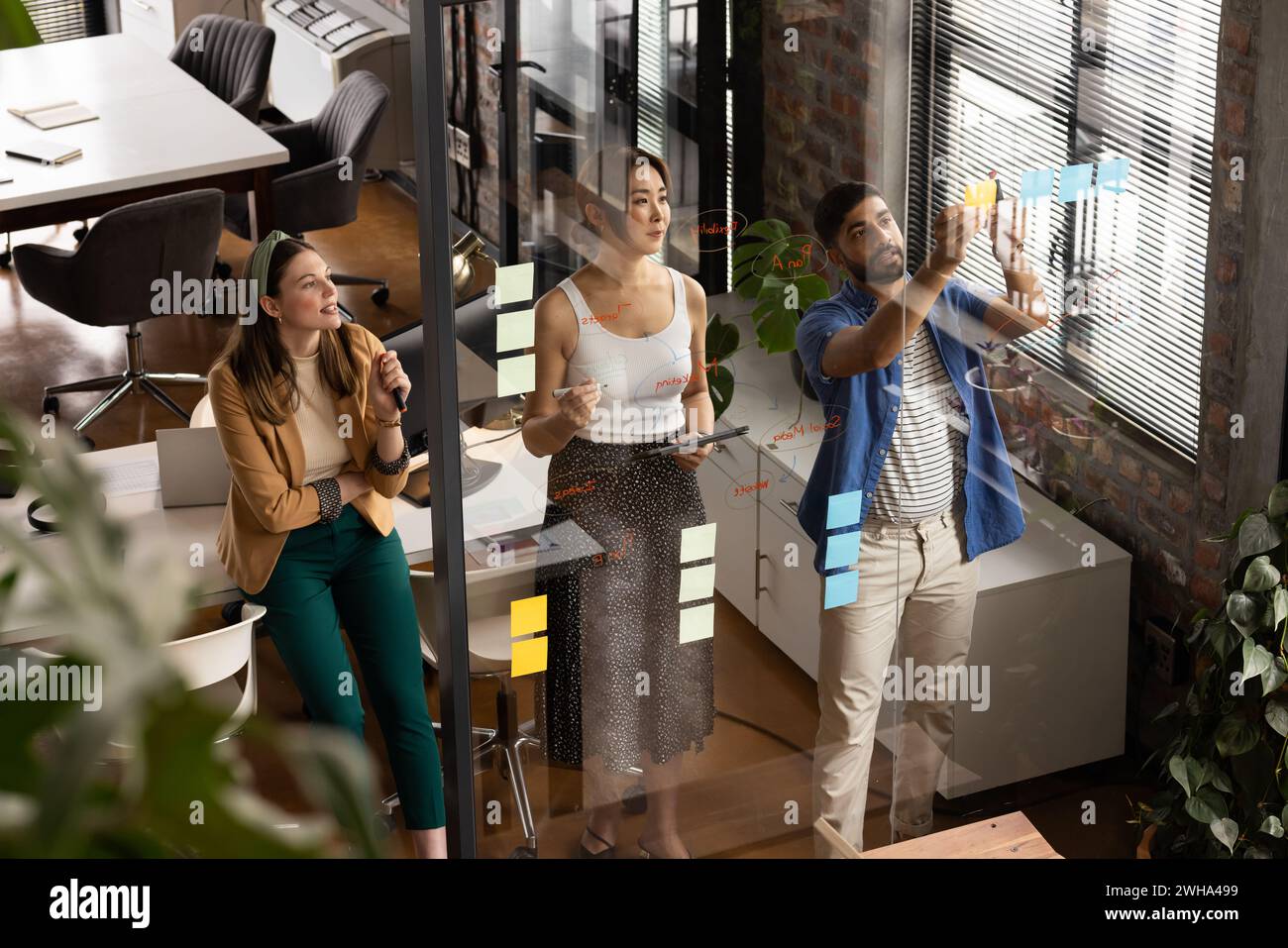 Young Asian man explains a concept on a glass wall in a casual business setting in the office Stock Photo