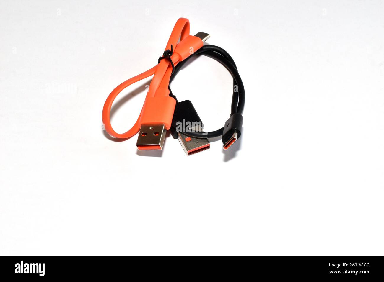 Orange and black USB cables twisted into rings lie on a white background. Stock Photo