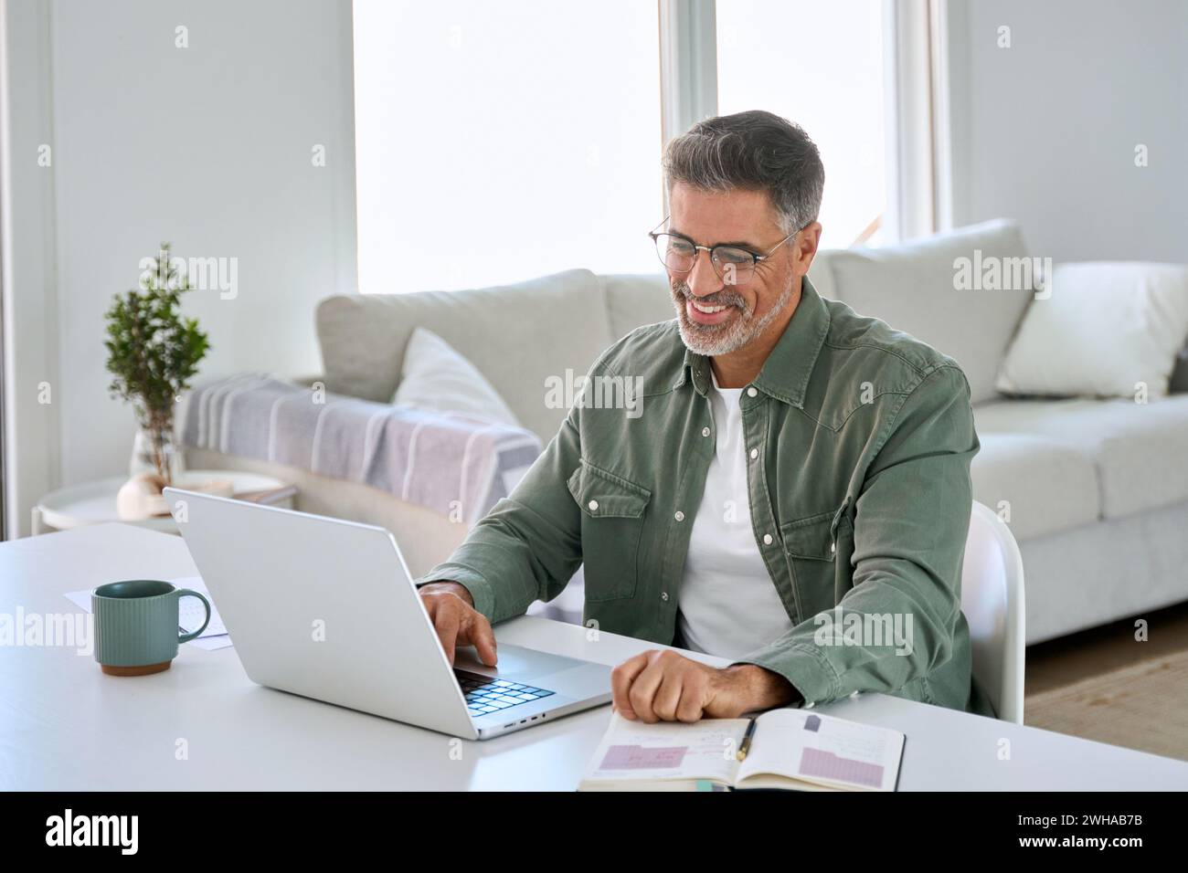 Happy older middle aged man using laptop computer at home table. Stock Photo