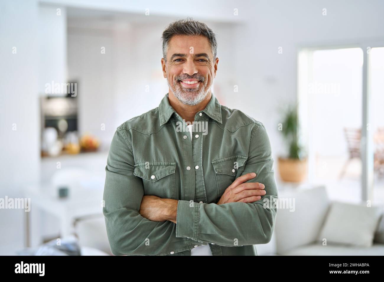 Happy middle aged senior man standing with arms crossed at home ...