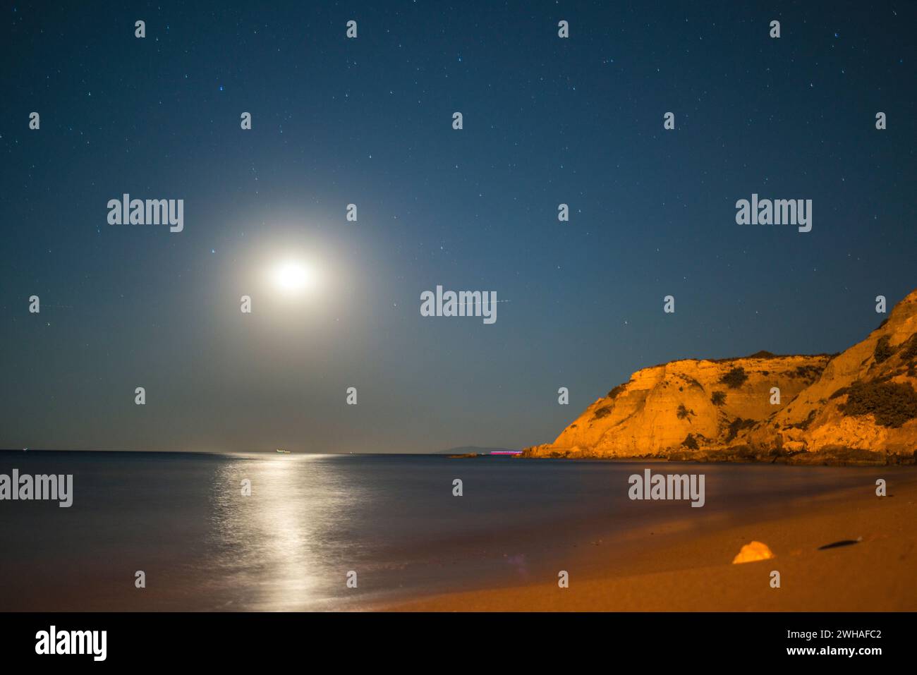 A serene coastal night illuminated by the full moon, casting a tranquil lunar glow over the calm sea and creating a majestic seaside beauty Stock Photo