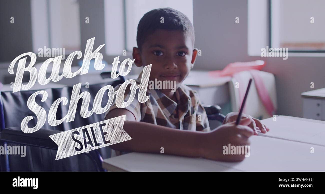 Image of back to school sale text over smiling biracial schoolboy working at desk in class Stock Photo