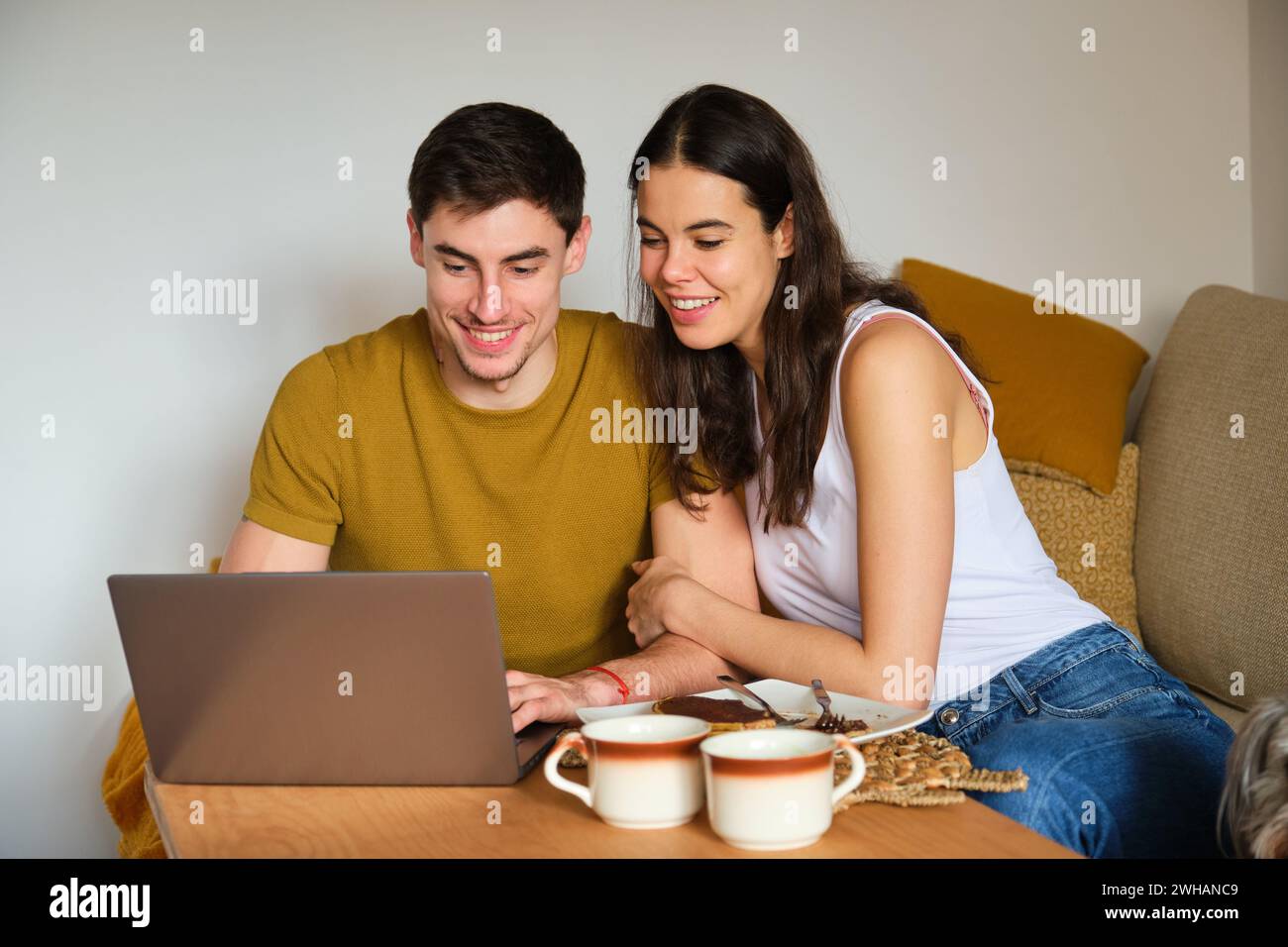 Happy couple using the laptop while having breakfast. Stock Photo