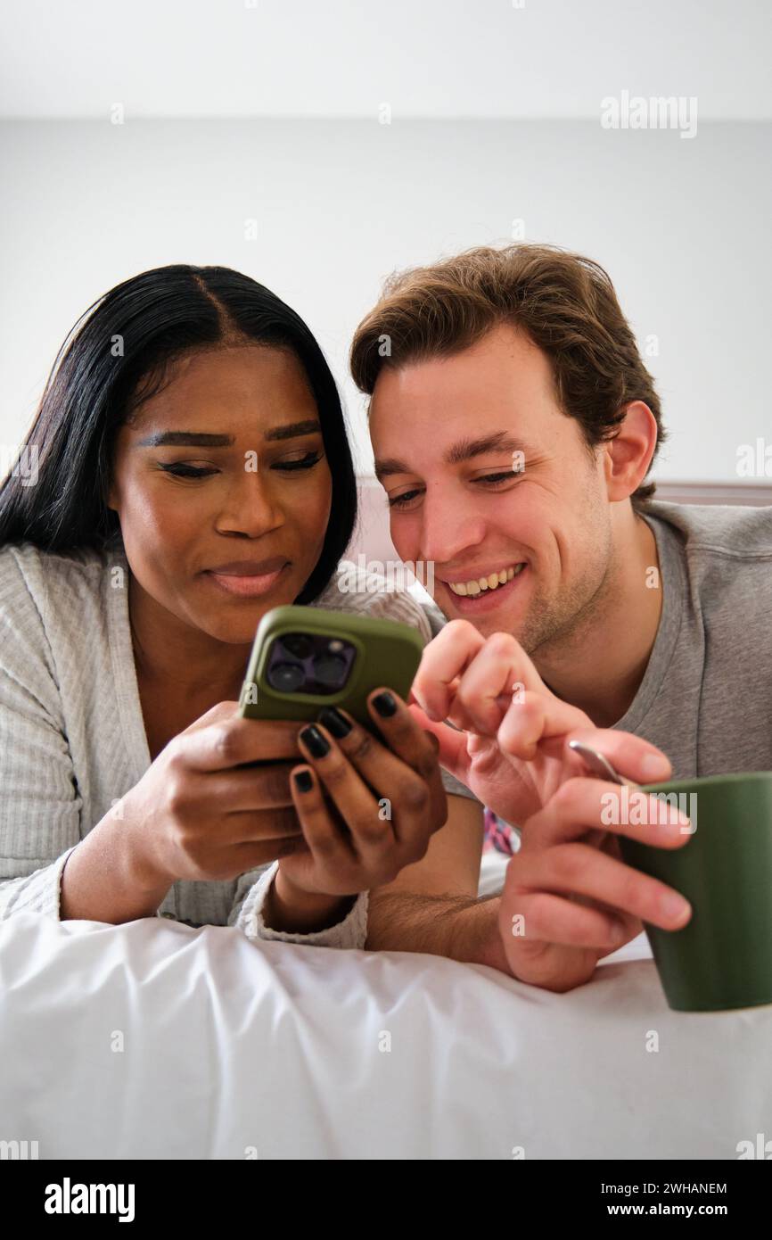 Multiethnic couple using the smartphone together on bed. Stock Photo