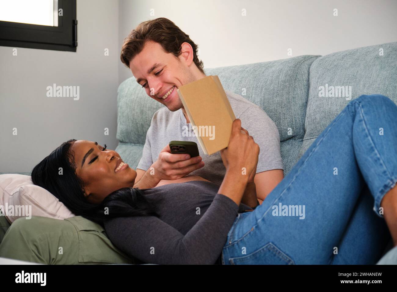 Multiethnic couple reading a book while rest in a sofa at home. Stock Photo