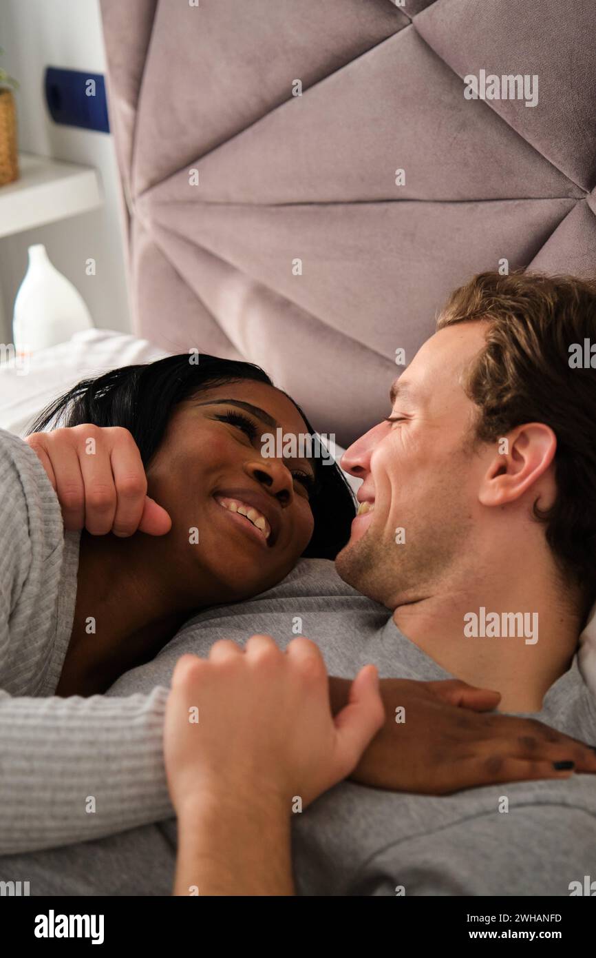 Multiethnic couple in love embracing and lying on bed. Stock Photo