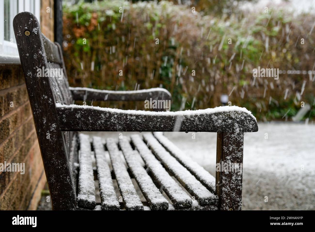 A side view of a wooden bench covered in a dusting of snow Stock Photo