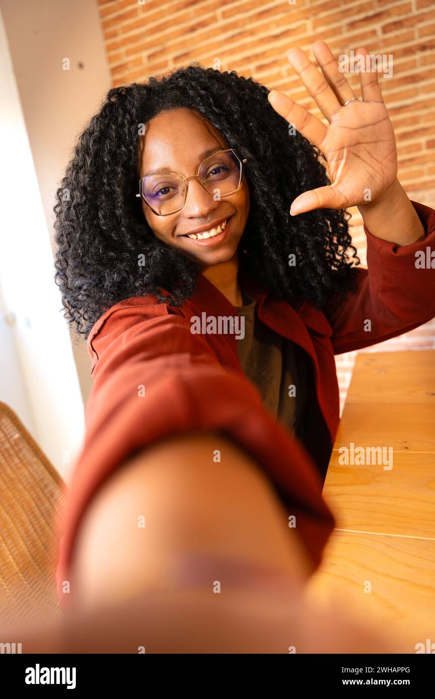 Beautiful woman with glasses curly hair smiling making a self portrait indoors. Vertical Stock Photo