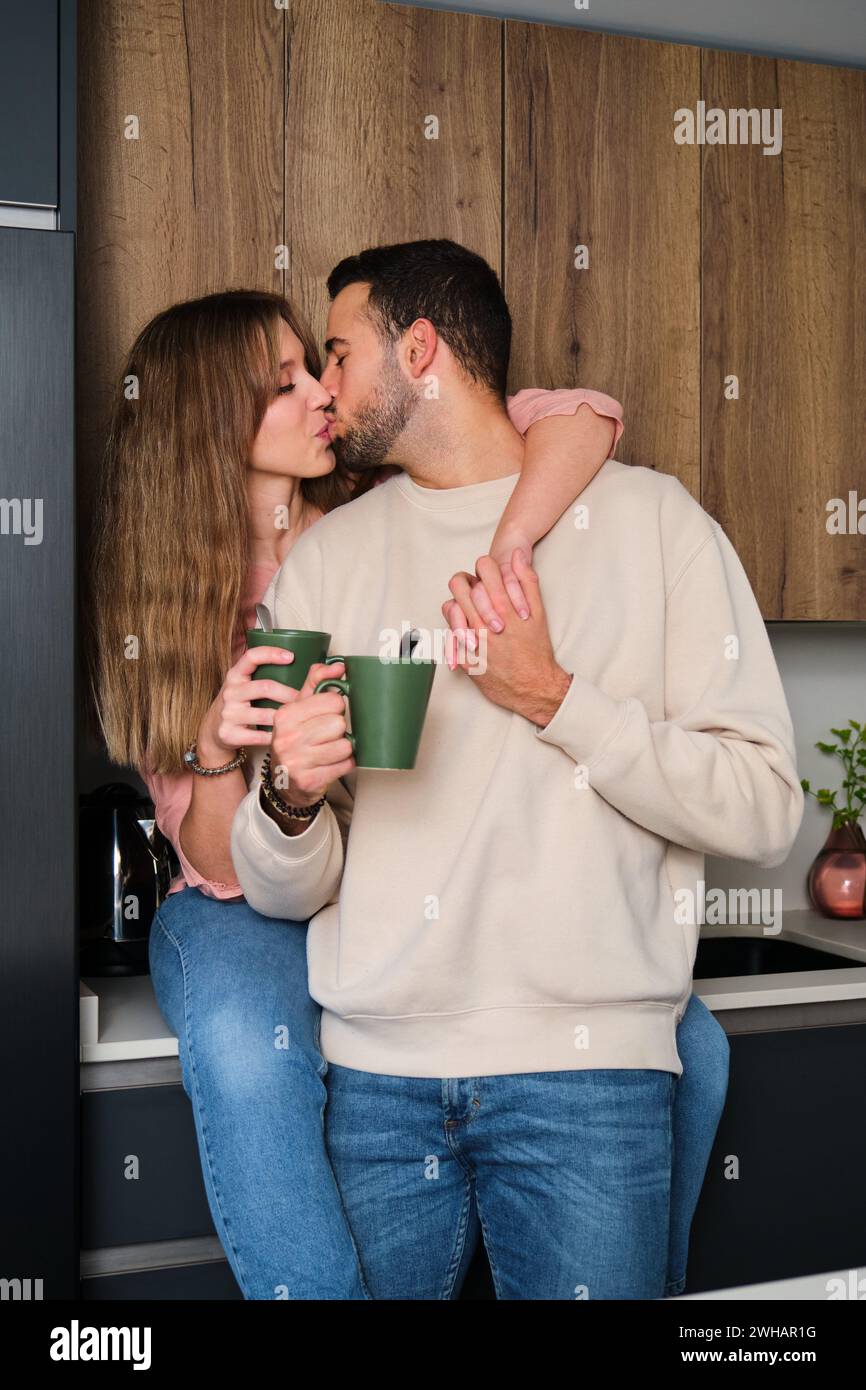 Spanish young couple kissing while having a coffee in kitchen. Stock Photo