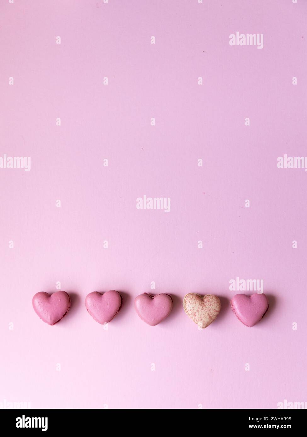 Five heart shaped pink macarons on bright pink backdrop Stock Photo