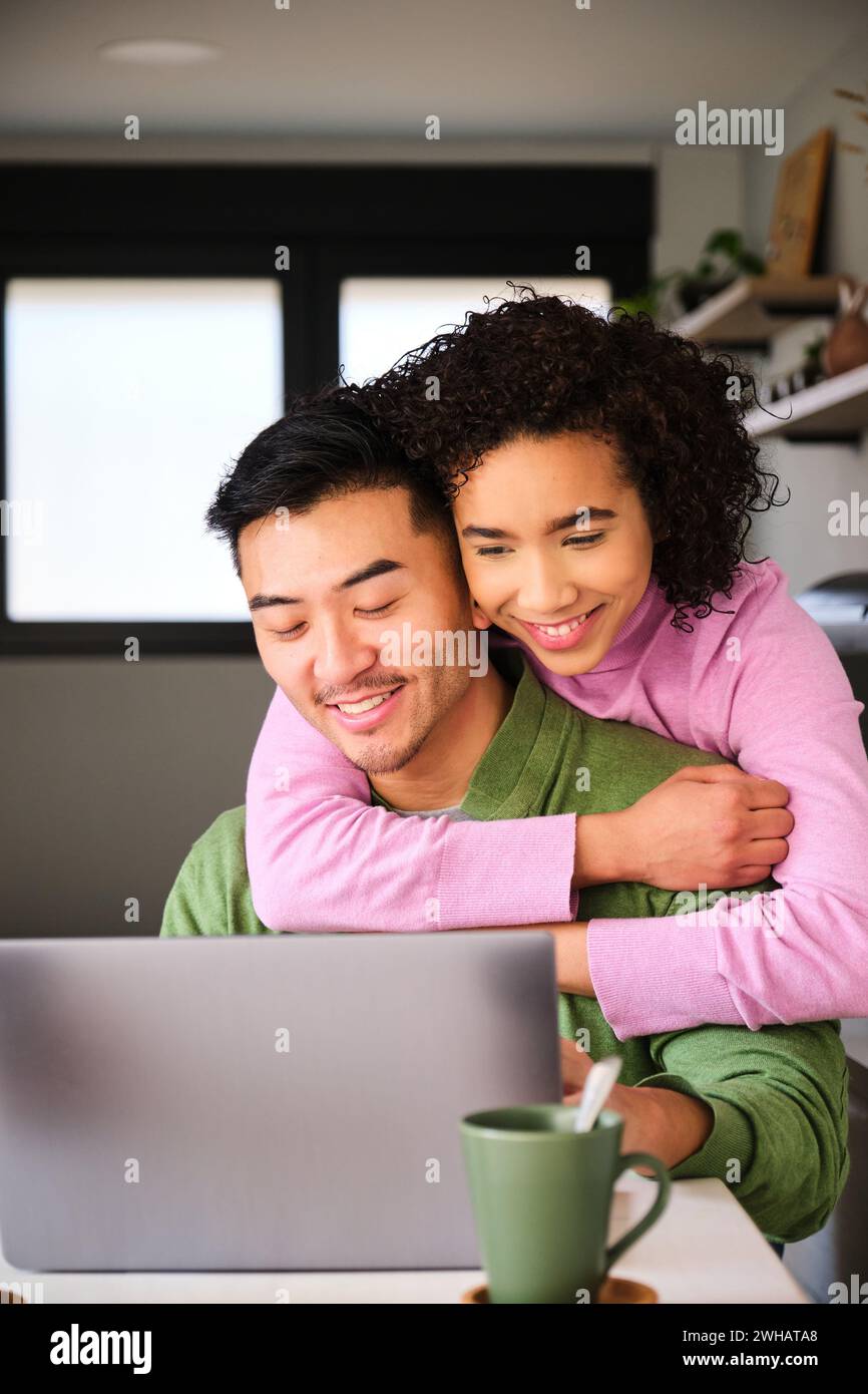 Multiracial happy couple using the laptop and hugging. Stock Photo