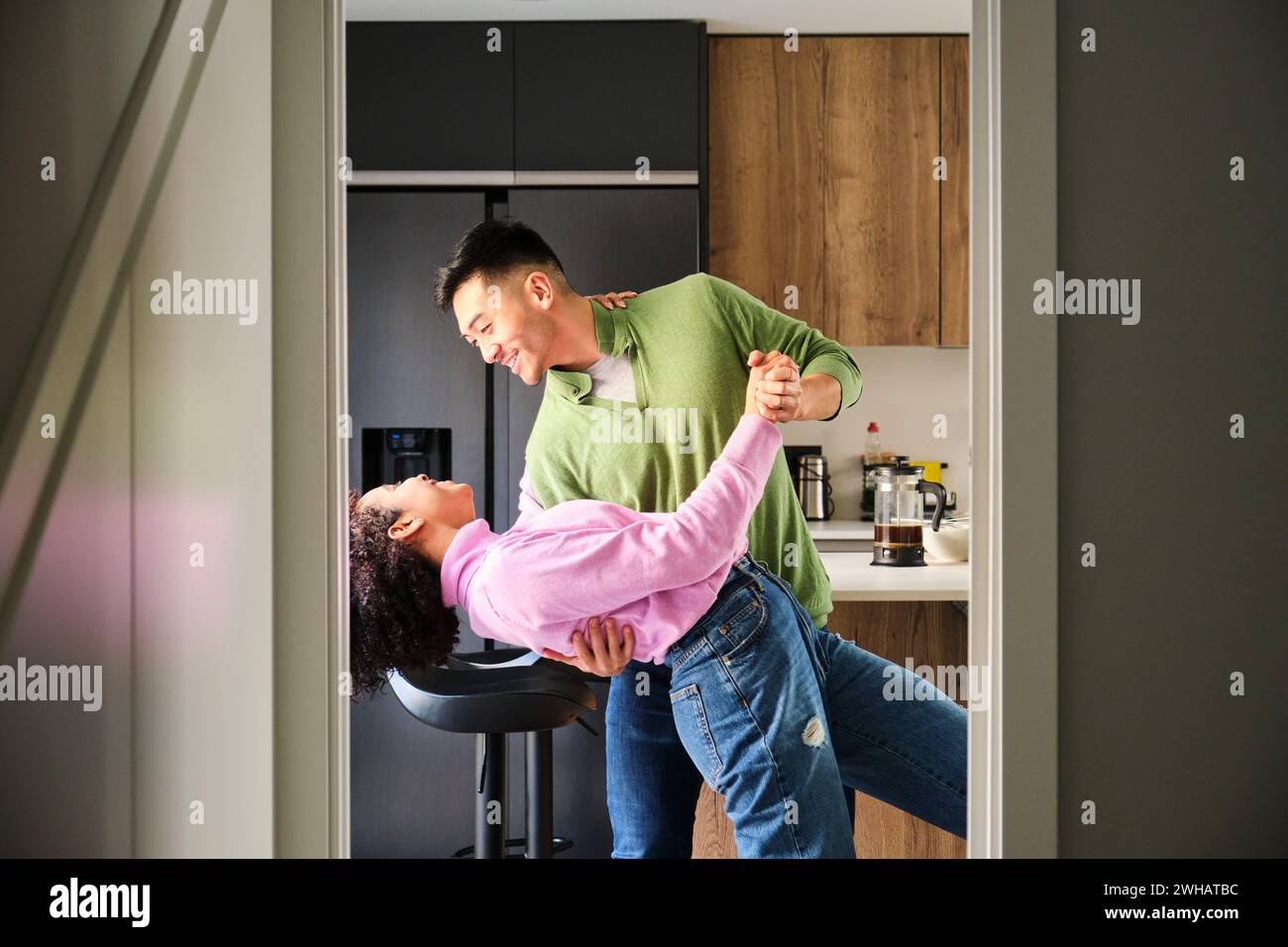 Multiethnic happy couple dancing in kitchen. Stock Photo