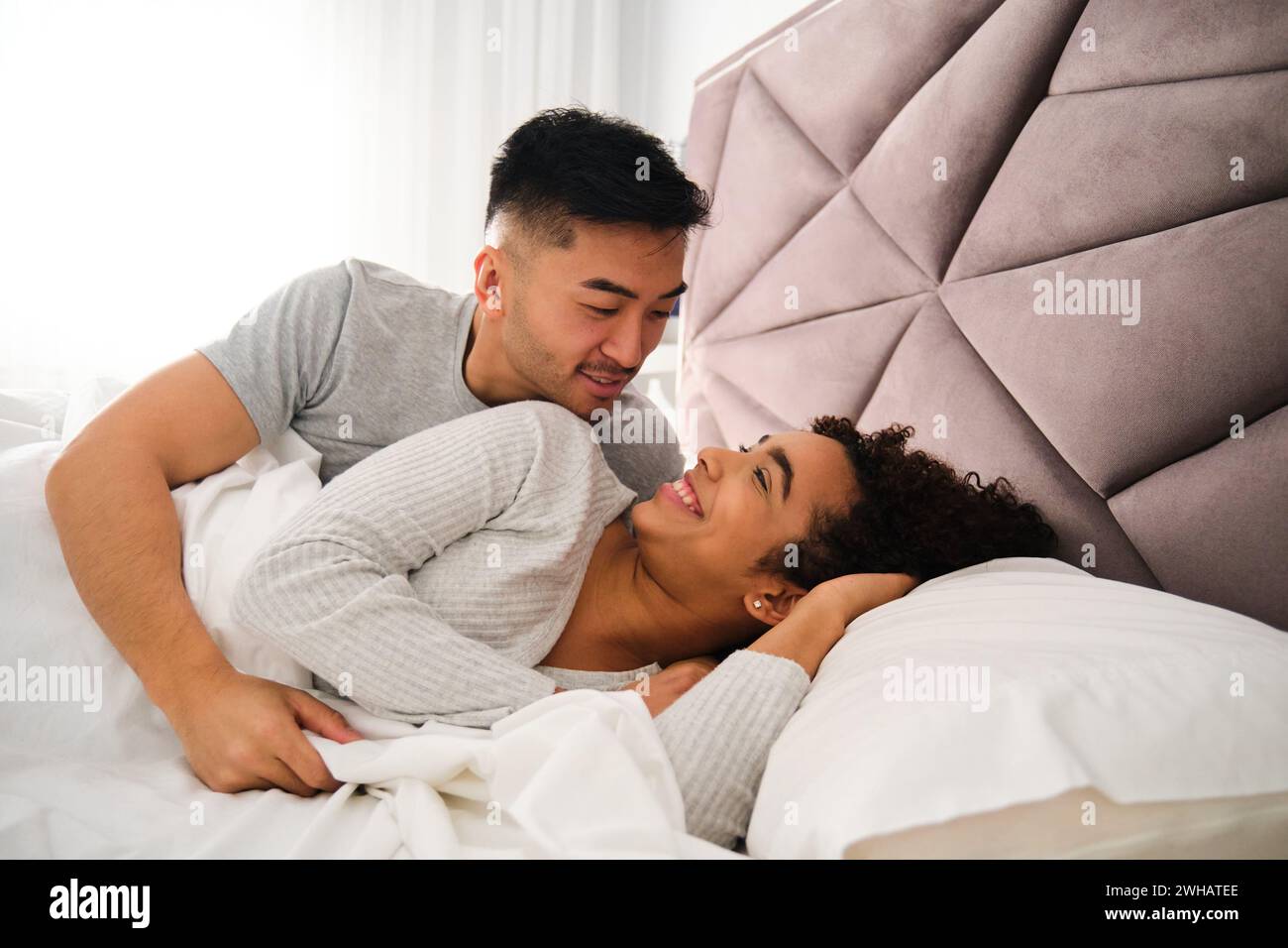 Multiracial romantic couple wake up together in bed during honeymoon. Stock Photo