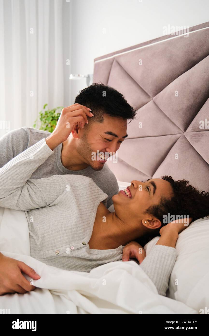 Diverse romantic couple wake up together in bed during honeymoon. Stock Photo
