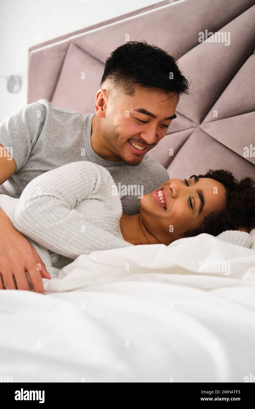 Multiracial romantic couple wake up together in bed during honeymoon. Stock Photo