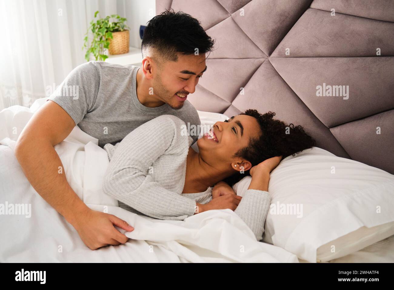 Multiethnic romantic couple wake up together in bed during honeymoon. Stock Photo