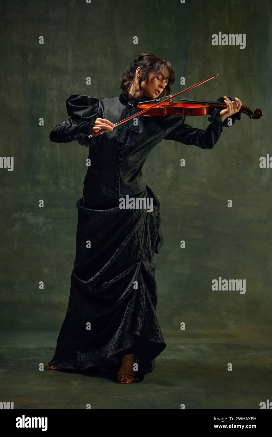 Dynamic pose of passionate female musician, young woman, violinist in black attire, playing