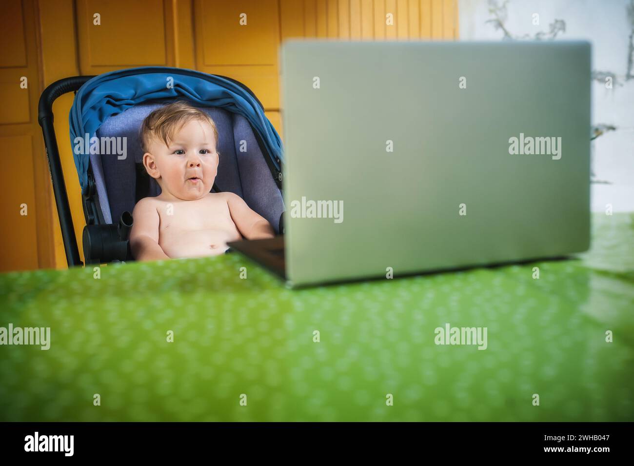 Happy baby boy sitting and watching cartoons on modern wireless computer laptop. The child smiles in a cheerful mood Stock Photo