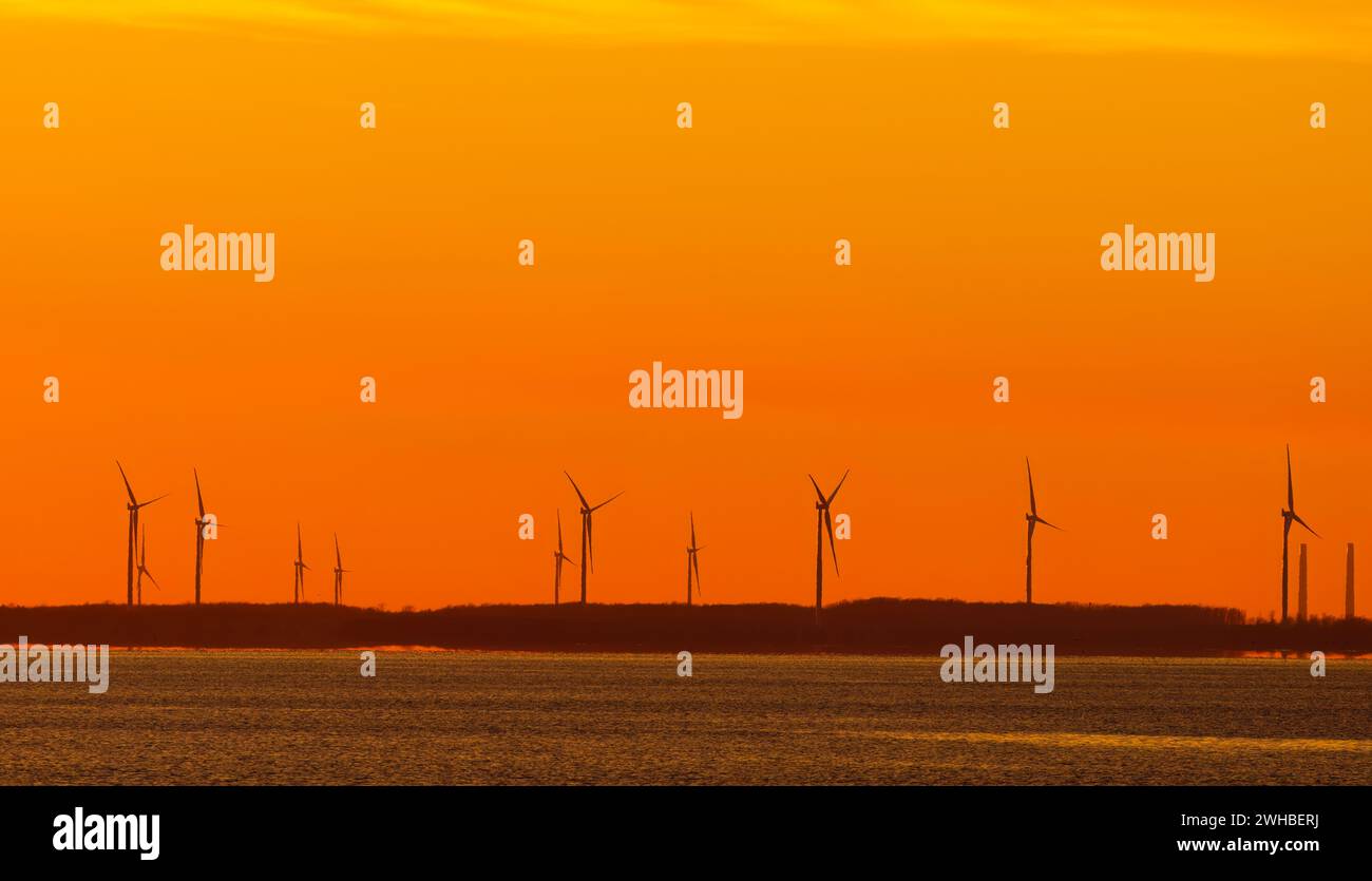Wind turbines below an orange sky sunset in winter on Amherst Island, Ontario, Canada Stock Photo