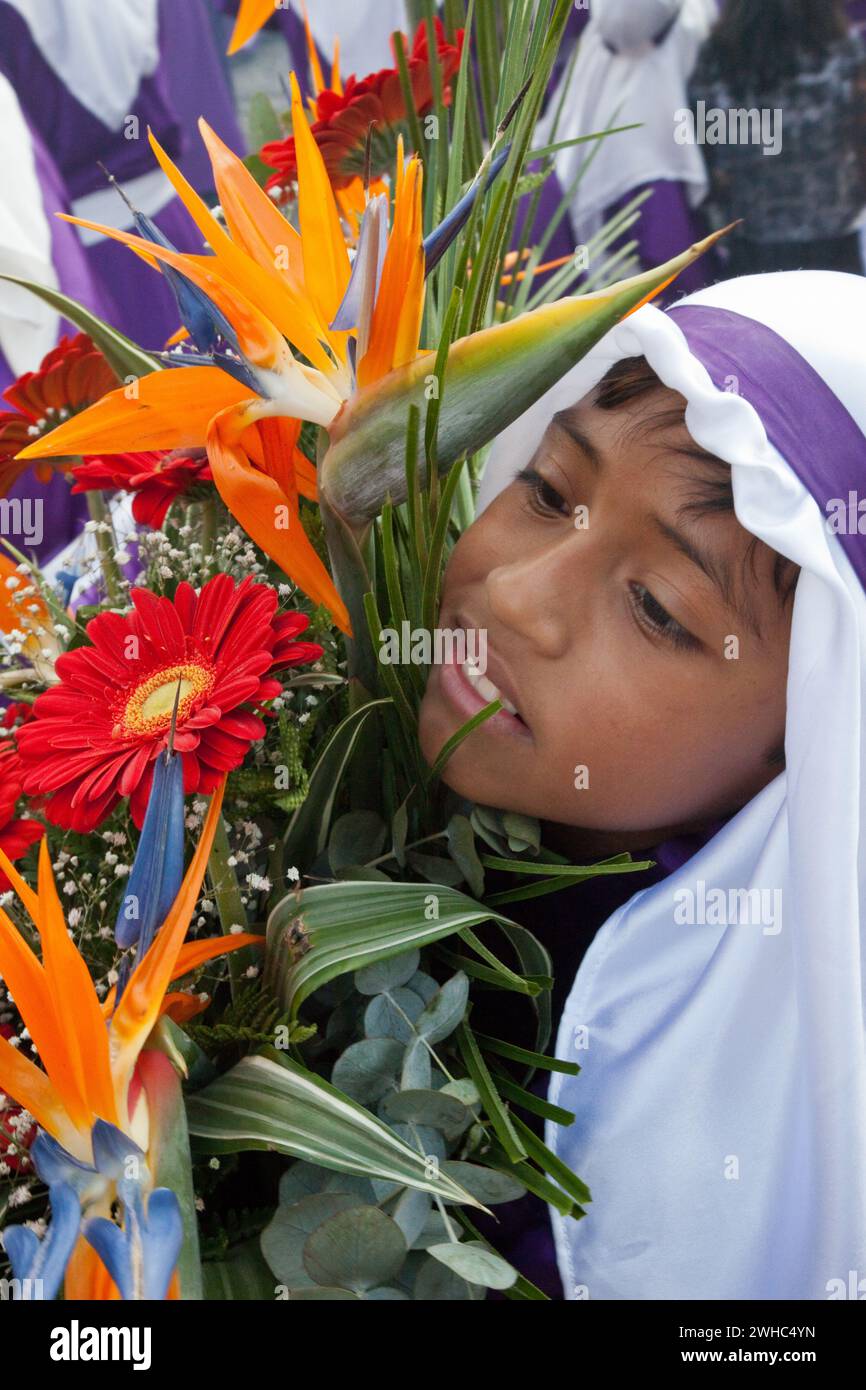 Antigua, Guatemala.  Young Cucurucho Carrying Large Vase of Flowers as he Accompanies a Procession during Holy Week, La Semana Santa Stock Photo