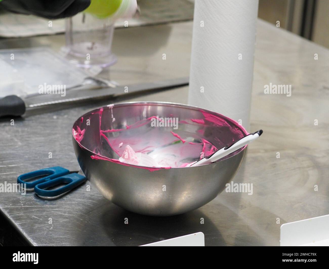 A mixing bowl with remnants of pink icing and a spatula on a kitchen