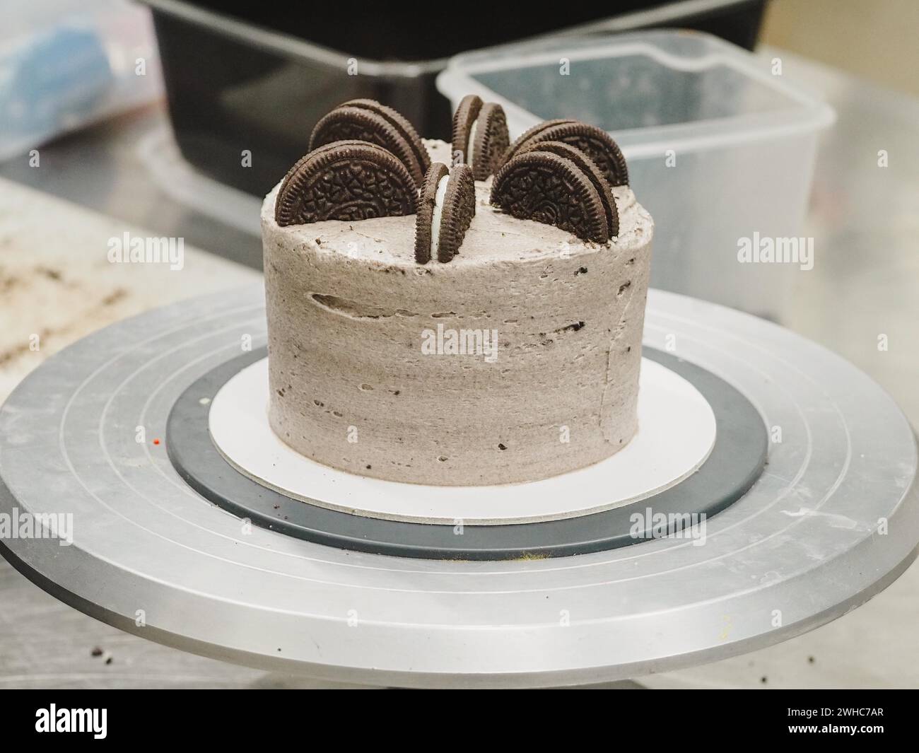Dark chocolate cookies topping a cream cake with whole Oreos on top, on a kitchen turntable Stock Photo