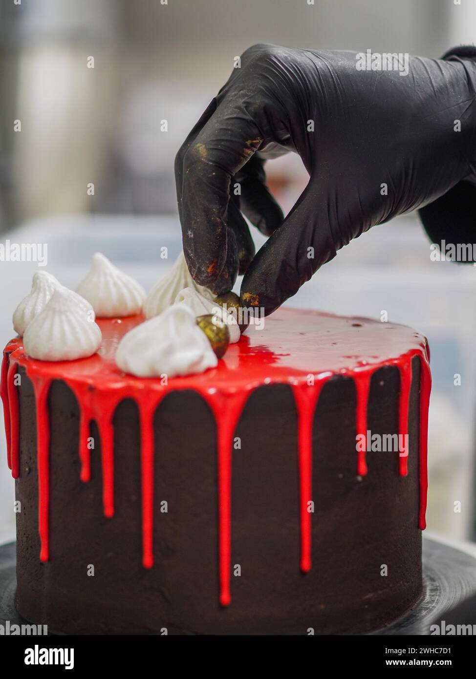 Pastry chef Gloved hand delicately placing a gold-colored chocolate ...