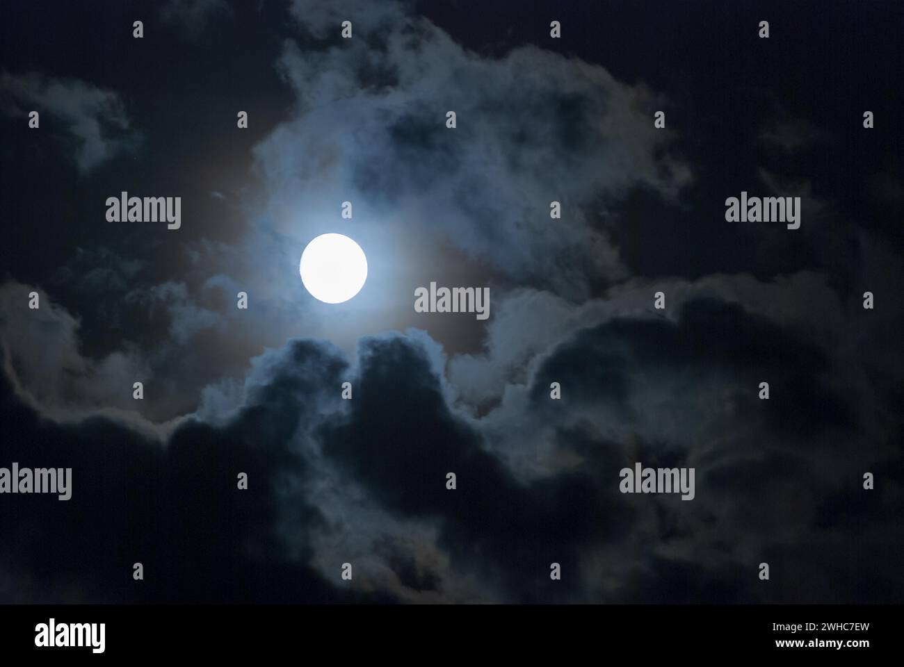 The full moon shines brightly in a cloudy, stormy, black sky and has a ...