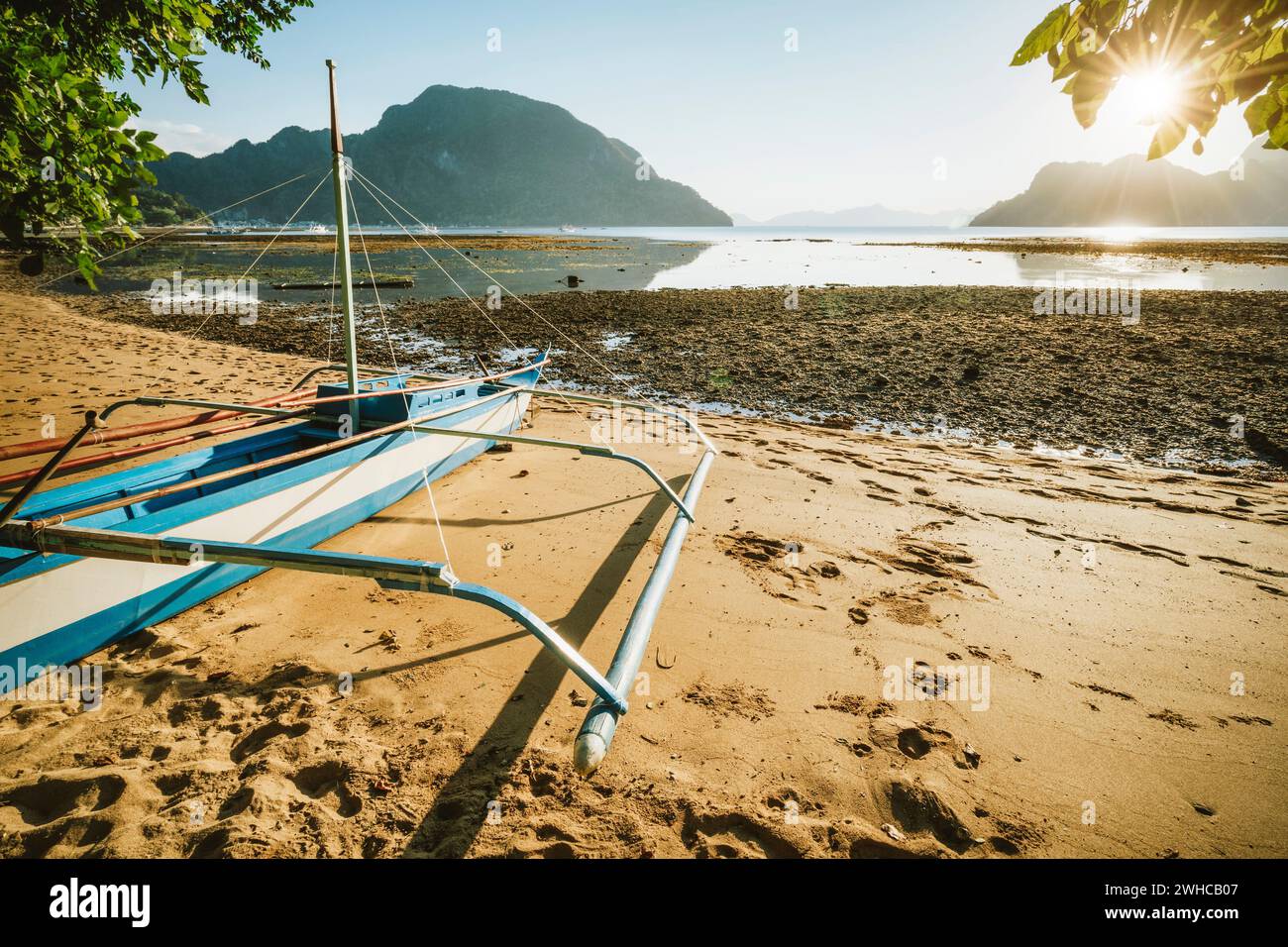 Bangka boat on sandy beach with golden sunset light over tropical islands in background. El Nido bay. Philippines. Stock Photo