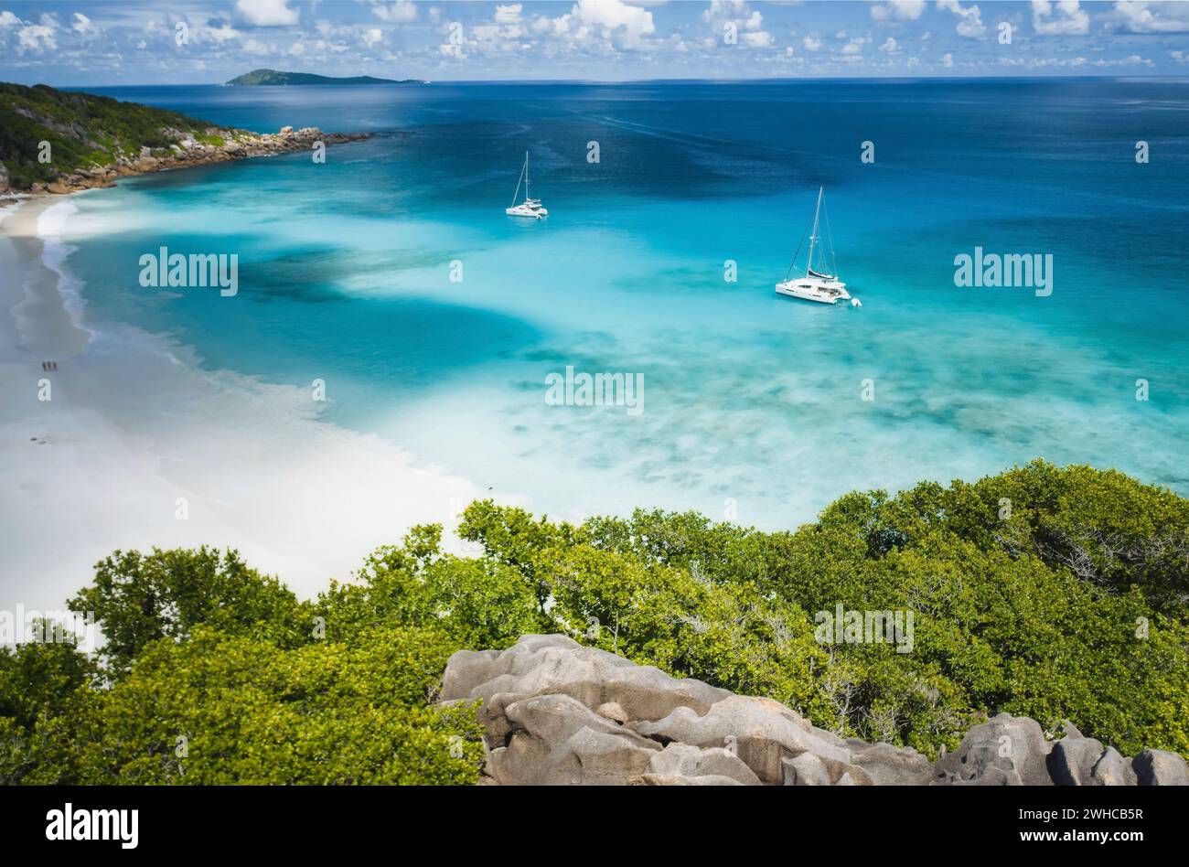 Aerial of Grand Anse beach at La Digue island in Seychelles. White sandy beach with blue ocean lagoon and catamaran yacht moored. Stock Photo