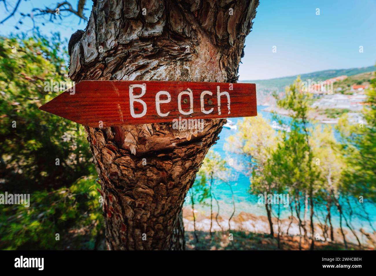 Assos village in morning light, Kefalonia. Greece. Beach wooden arrow sign on a pine tree showing direction to small hidden beach. Stock Photo