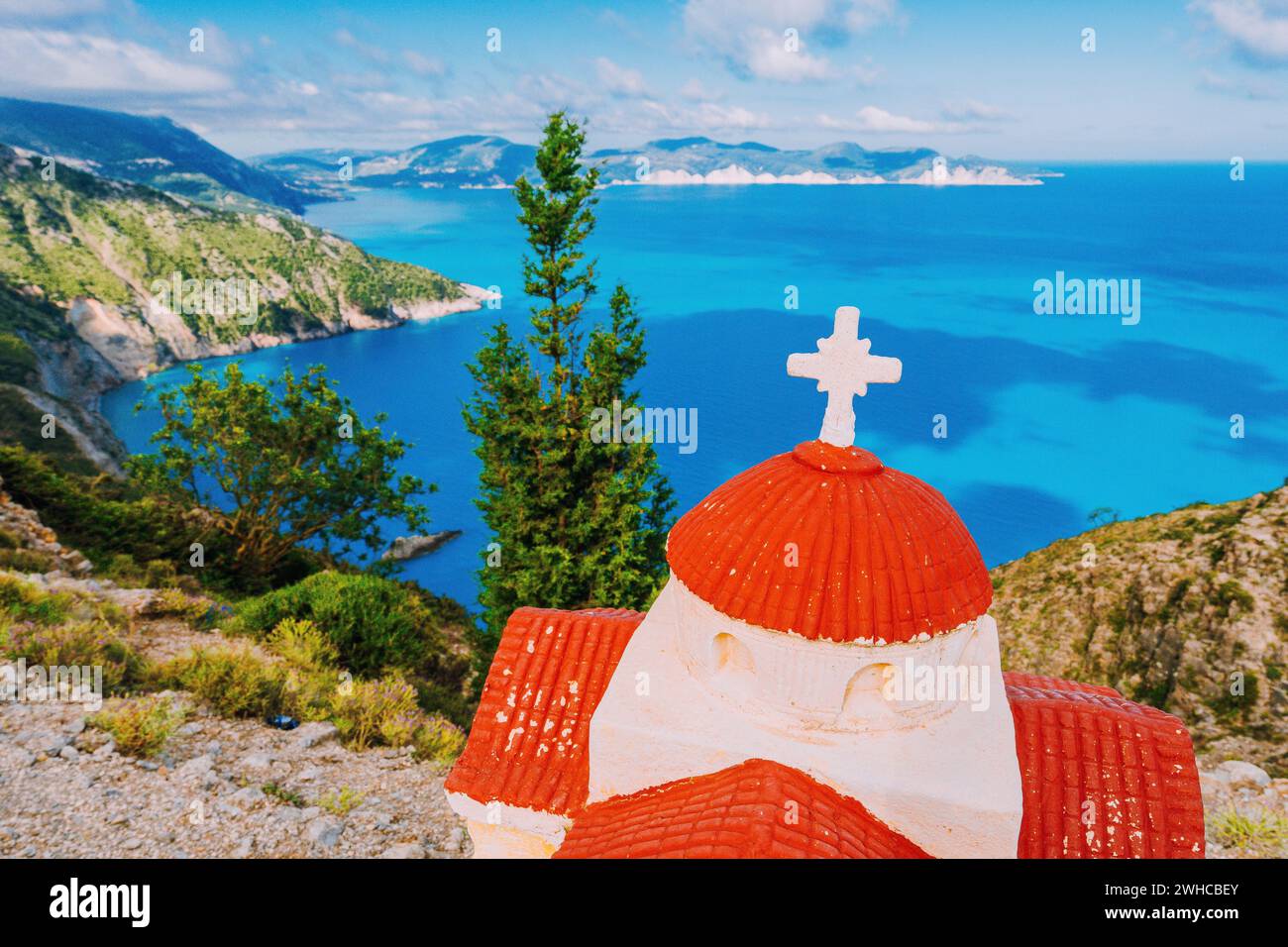 Orange colored Hellenic shrine Proskinitari on the cliff edge with defocused sea and cloudscape view in the background. Stock Photo