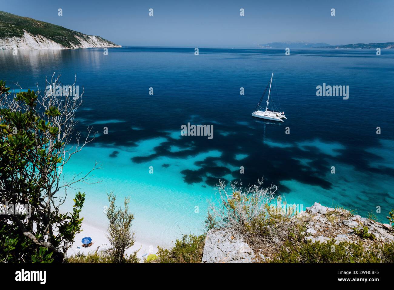 Fteri beach, Cephalonia Kefalonia, Greece. White catamaran yacht on clear transparent blue azure sea water surface. Paradise beach. Stock Photo