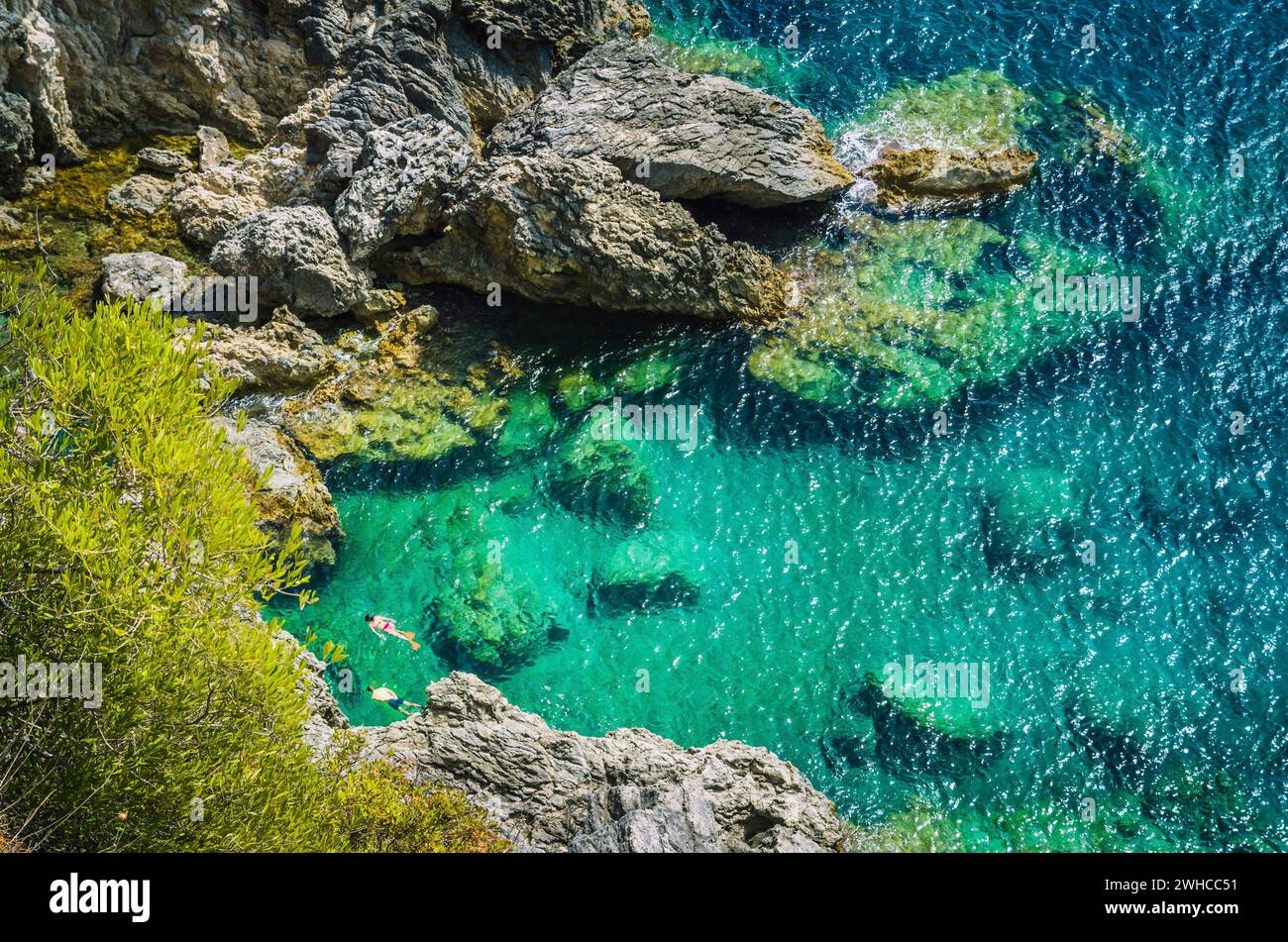 Tourists shorkling between Rocks in Azure Bay of Beautiful Paleokastritsa in Corfu Island, Greece. Stock Photo