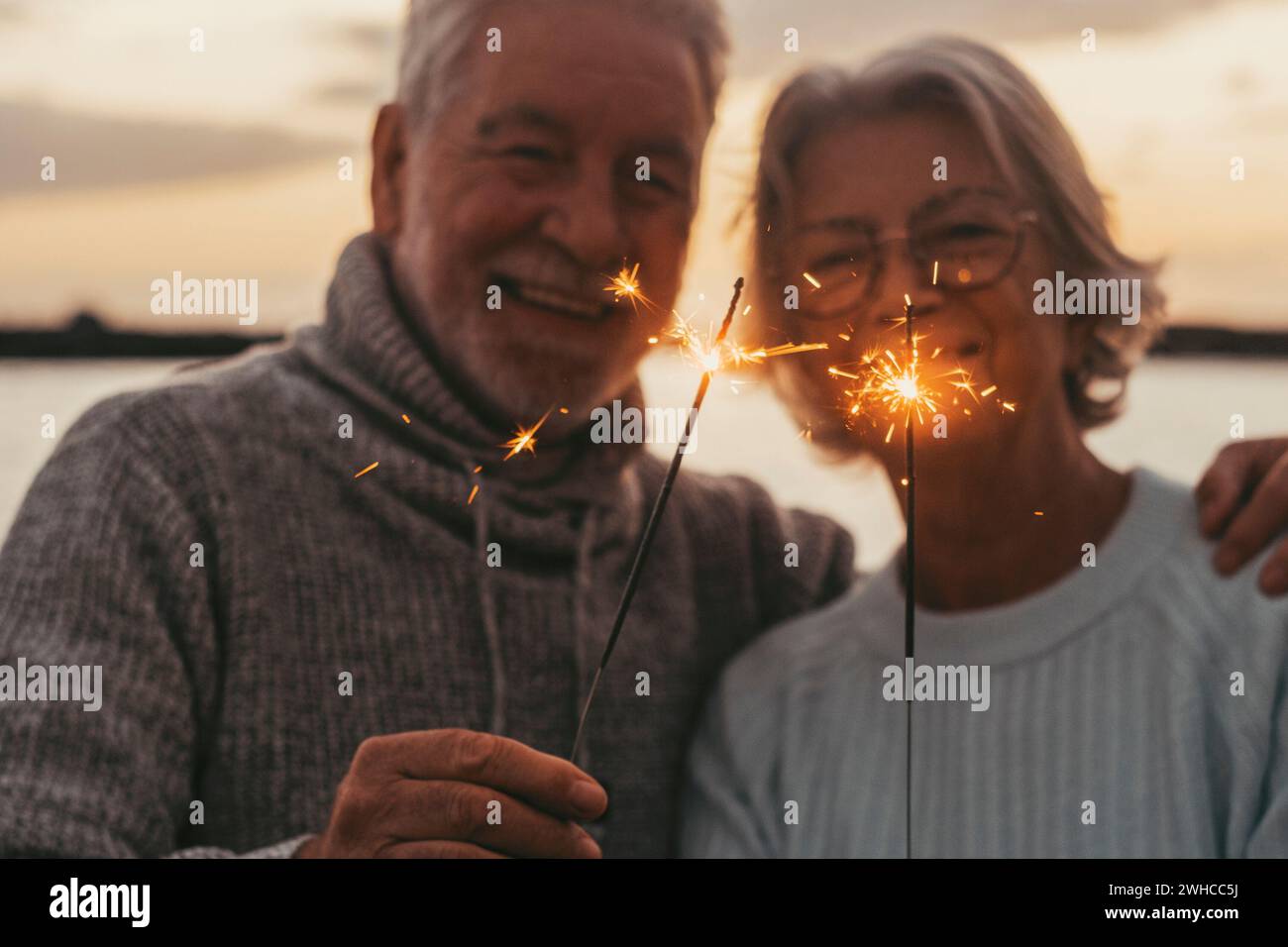 Couple of two old seniors holding sparklers lights at the evening at the beach together enjoying and having fun Stock Photo