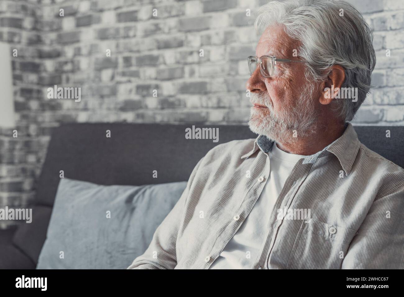 Face of senior caucasian hoary man looking away deep in sad thoughts feels lonely close up portrait, recollect memories and life moments, depressed grandfather alone indoors, yearning for wife concept Stock Photo