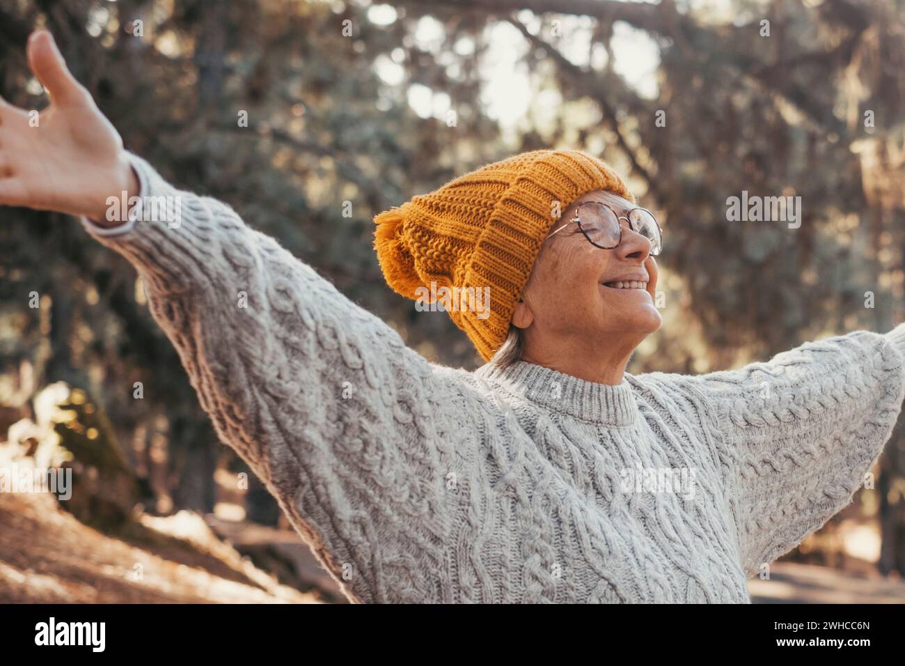 Portrait, close up of middle age woman enjoying and relaxing sitting at table in the nature in the forest of mountain. Old female person opening arms and closing eyes feeling free. Freedom concept lifestyle. Stock Photo