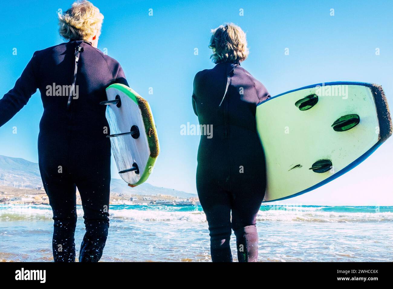 happy and healthy seniors enjoying summer and vacations outdoors at the beach entering to the water with wetsuits and surfboards - pensioners and retired go surfing Stock Photo