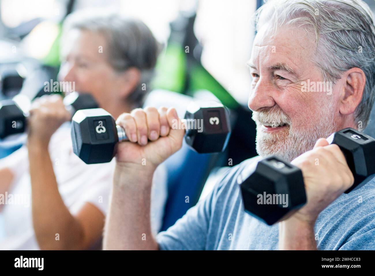 mature man with his wife doing exercise of biceps at the gym - fitness and healthy lifestyle concept - training their body together - couple of two seniors Stock Photo