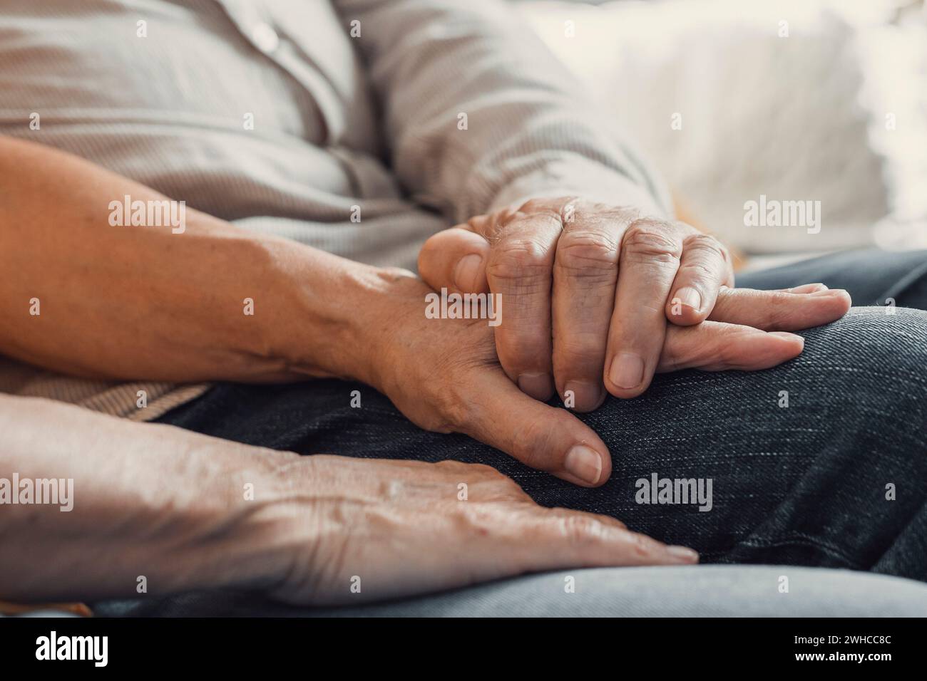 Close up elderly affectionate woman covering wrinkled hands of mature husband, showing love and support at home. Caring middle aged family couple enjoying sincere trustful honest conversation. Stock Photo