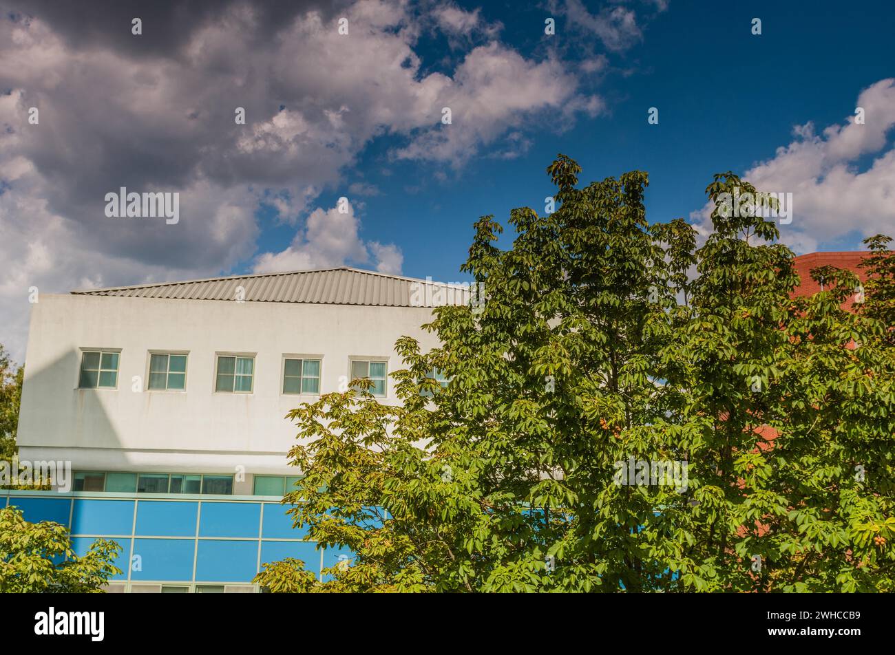 Blue cloudy sky over a large building on a summer day with trees in foreground Stock Photo
